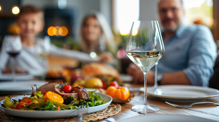 Family gathering around a table to share a Thanksgiving meal, with focus on a beautifully plated dish and glass of wine.