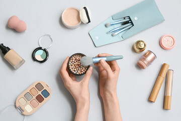 Female hands with powder pearls, makeup brush and different cosmetic products on grey background