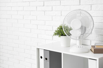 Electric fan, houseplant and book on shelving unit in office