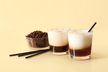 Glasses of White Russian cocktail and bowl with coffee beans on yellow background