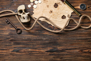 Burnt paper with skull, compass, coins and rope on wooden background. Pirate concept
