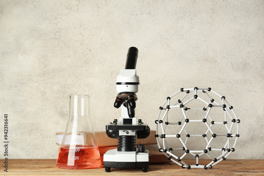 Wall mural modern microscope with chemical flask, molecular model and books on wooden table against white grung