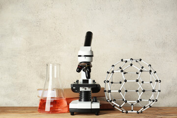 Modern microscope with chemical flask, molecular model and books on wooden table against white...