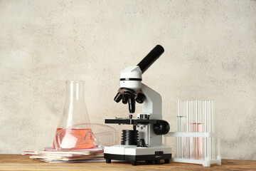 Modern microscope with chemical flasks, protective glasses and notebooks on wooden table against...