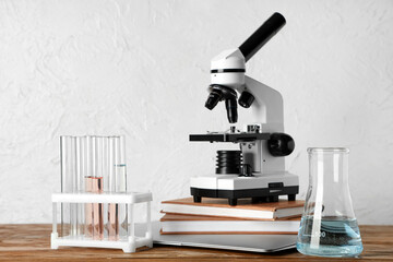 Modern microscope with chemical flasks and books on wooden table against white grunge background