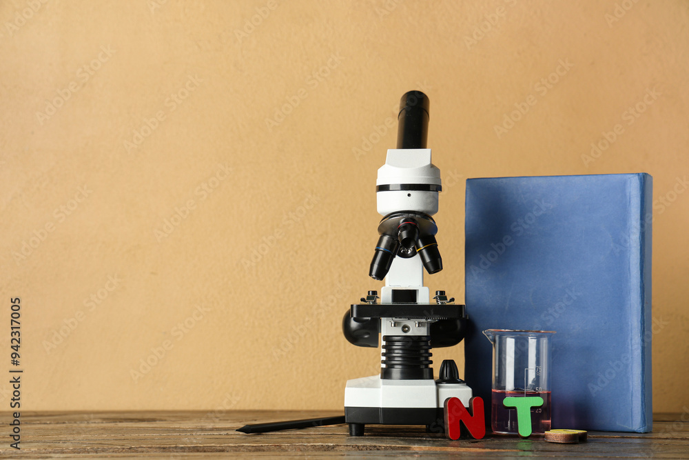 Wall mural Modern microscope with chemical flask and book on wooden table against beige background