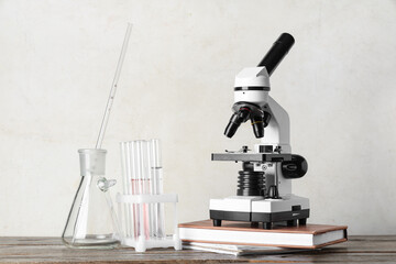 Modern microscope with chemical flasks and book on wooden table against white grunge background