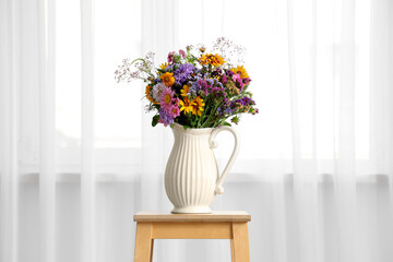Vase with wild flowers on stool near light curtains in room. Closeup