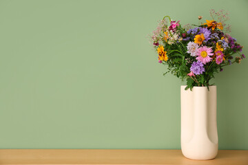 Vase with wild flowers on table near green wall in room. Closeup
