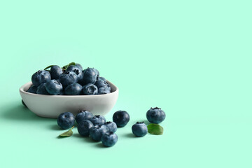 Bowl with ripe blueberry on turquoise background, closeup