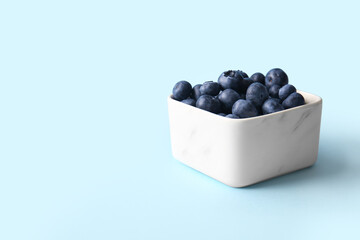 Square bowl with fresh ripe blueberry on blue background, closeup