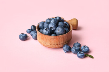 Wooden bowl and scoop of fresh ripe blueberry on pink background, closeup
