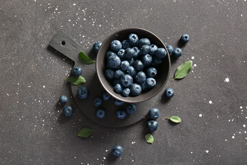 Cutting board and bowl with fresh ripe blueberry on black background
