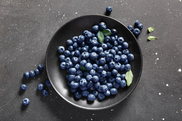 Plate with fresh ripe blueberry on black background