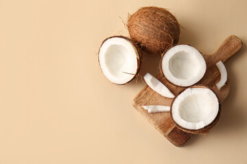 Wooden board with fresh coconuts on beige background