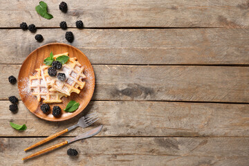Delicious Belgian waffles with blackberries and sugar powder on plate on wooden background. Top view