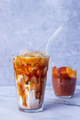 a glassof ice caramel macchiato coffee with straw glass on white marble table.