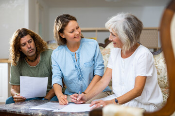 Obraz premium Mature woman at table in home room filling up documents with family