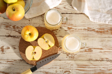 Mason jars of fresh apple kvass and fruits on white wooden background