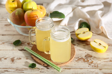Mason jars of fresh apple kvass and glass bowl with fruits on white wooden background
