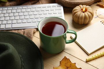 Cup of tea with hat, notebook and computer keyboard on wooden table, closeup