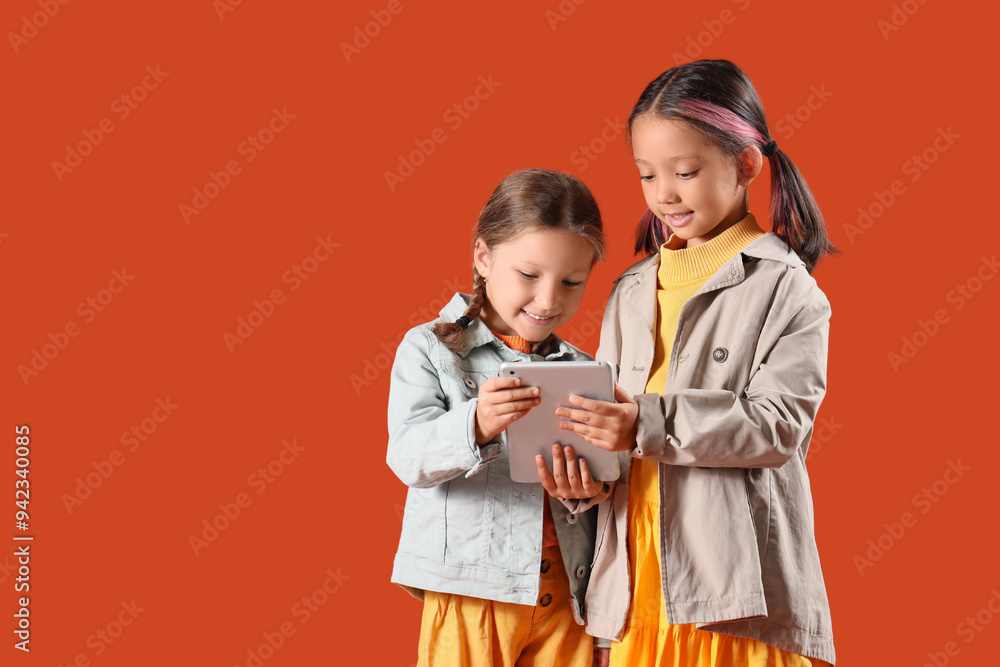 Poster cute little happy girls in autumn clothes with tablet on orange background