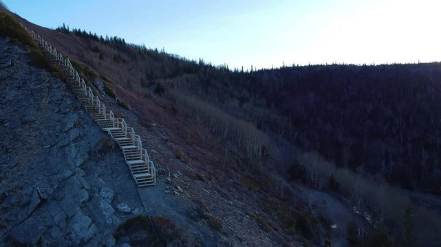 Un drone survol un escalier de montagne en bois endommag&eacute; aboutissant a une croix en m&eacute;tal sur une falaise rocheuse parsem&eacute; de v&eacute;g&eacute;tation au sommet du Mont Saint-Pierre, Gasp&eacute;sie, Qu&eacute;bec.