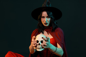 Beautiful young woman dressed as witch for Halloween with human skull on black background