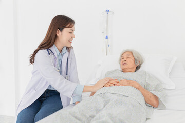 Asian female doctor comforting elderly patient in hospital bed. Healthcare professional showing...