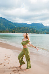 Cute blonde girl in a green suit poses on the beach against the background of the mountains, Kauai, Hawaii