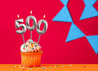 Birthday cupcake with candle number 500 on a red background with blue pennants