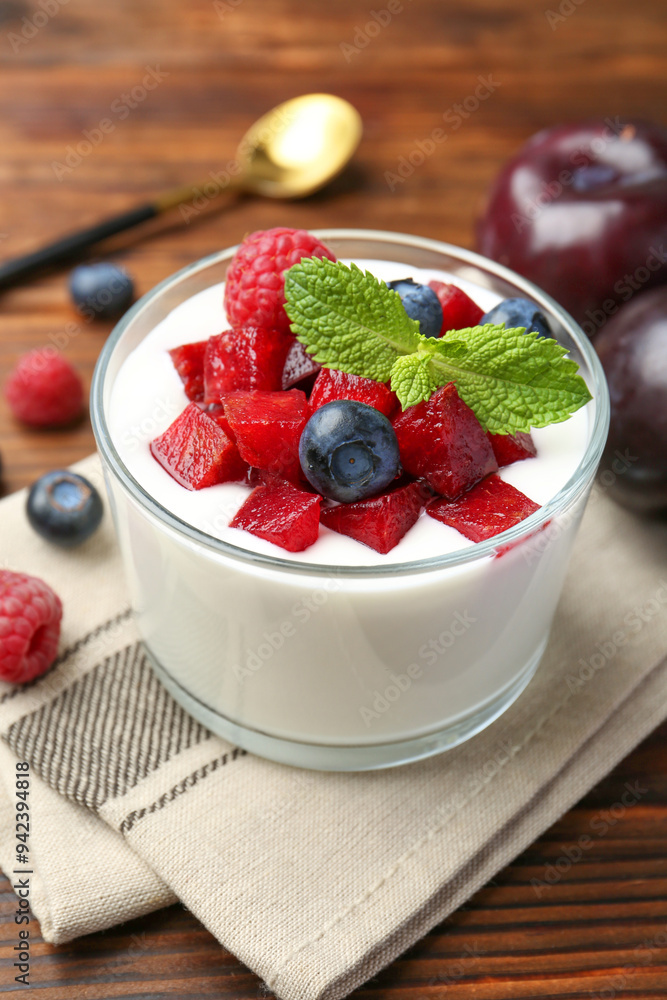 Poster Tasty yogurt with fresh plums, berries and mint in glass on wooden table, closeup