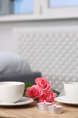 Burning candles, two cups of drink and flowers on wooden table indoors. Space for text