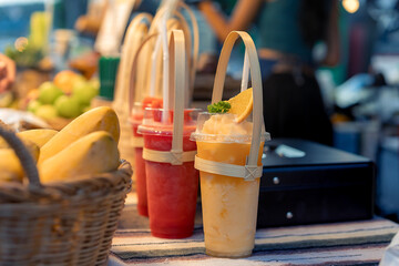 Young Asian woman makes smoothies and colorful fresh fruits at a health-conscious juice bar. which promotes health and nutrition, watermelon smoothie and orange smoothie, mango in a wicker basket.