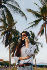 Woman in sunglasses talking on a cell phone with palm trees in the background on a sunny day