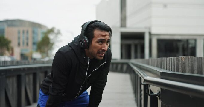 Man, rest and runner in outdoor as tired in exercise, workout and training by running in Netherlands. Male person, cardio and jogging for fitness, strong muscle or wellness with headphones as athlete
