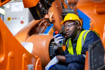 African American man engineer standing holding walkie talkie at automation robot arms machine in factory. repairman of welding robots in production. technology intelligence electronic innovation.