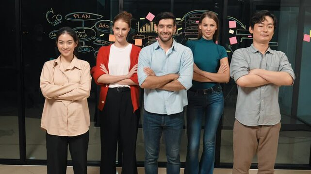 Professional business team crossing arms while standing together at glass wall. Group of businesspeople standing with arm folded while smiling at camera with confident in night office. Tracery