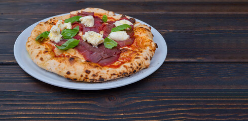 Italian Pizza Manzo in a plate on a wooden table. Space for text.