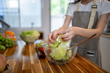 A close-up image of a woman preparing a salad bowl at the kitchen table, making healthy food at home