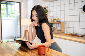 An attractive Asian woman is using her digital tablet at the kitchen table in her minimalist kitchen