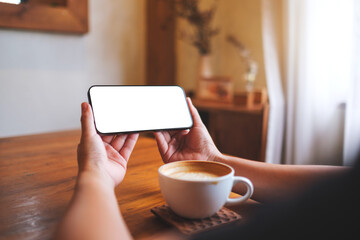 Mockup image of a woman holding and using mobile phone with blank desktop white screen at home
