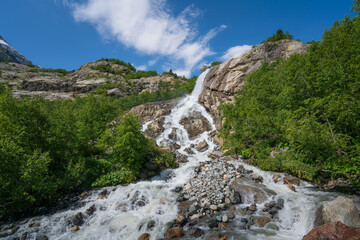 View of the Alibek waterfall formed by the fall of the Jalovchatka River from the Alibek glacier on a sunny summer day, Dombay, Karachay-Cherkessia, Russia