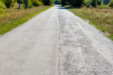 A road of local importance with two lanes of traffic, one half of which is covered with new asphalt to improve the safety of traffic. Half old, half new asphalt road