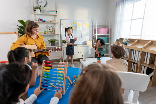Caucasian young woman teacher playing guitar with students in school.