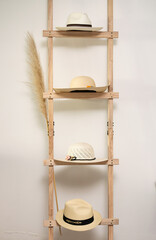 Light wooden ladder decorated with pink flowers and two toquilla straw hats with leather bands. Elegant composition blending traditional Ecuadorian craftsmanship, fashion, and rustic decorative style.