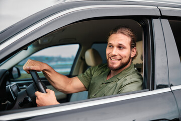 Smiling man driving a black car with confidence against an outdoor background