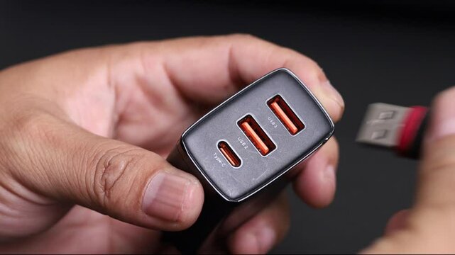 Inserting USB connector into the charger port closeup. USB connector system or connection interface in hand  on black background. Connecting USB Cable into a charger plugged. High quality 4K footage.