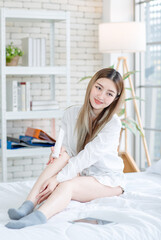 Asian young woman beautiful female happy smiling enjoying  with decorative makeup, beauty products, and cosmetics while sitting on white bed, Concept of teenage lifestyle at home