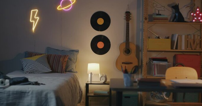 Zoom-in of stylish bedroom of teenager illuminated in evening with nobody inside. Modern apartment interior and accommodation concept.